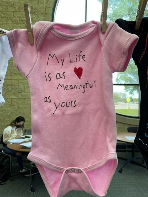 A baby onesie from the clothesline project reads, My life is as meaningful as yours.