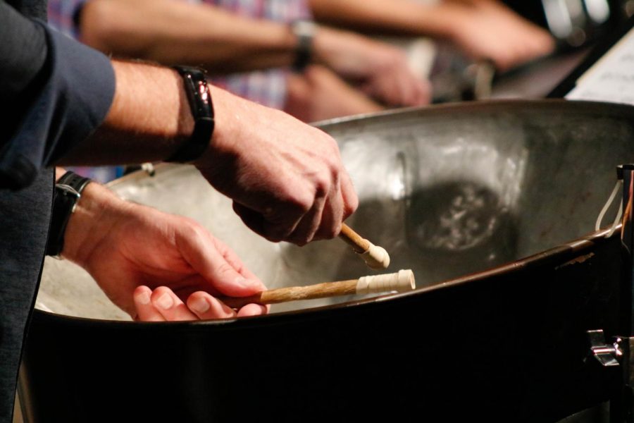 A pannist incorporates their mallet strikes into the bands musical arrangement. 