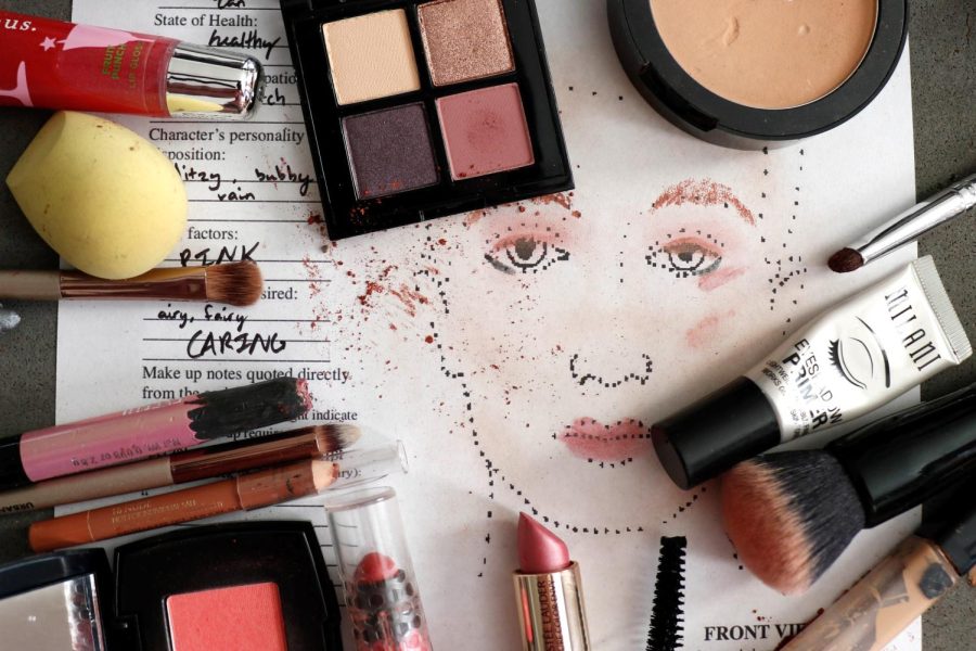Various types of makeup and makeup brushes sit atop a worksheet from a stage makeup class.