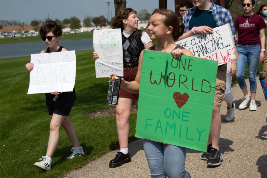 Kelly Stoffle, the HIA officer for PTK, at the Climate Refugee Walk holding a sign that says One world, one family.