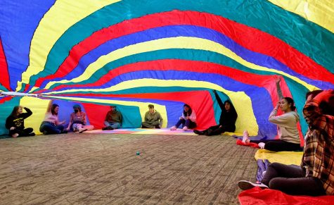 Students sit beneath the cover of a rainbow parachute at Recess Day on Nov. 15. They duck under the colors to relive and reminisce about their childhood. 