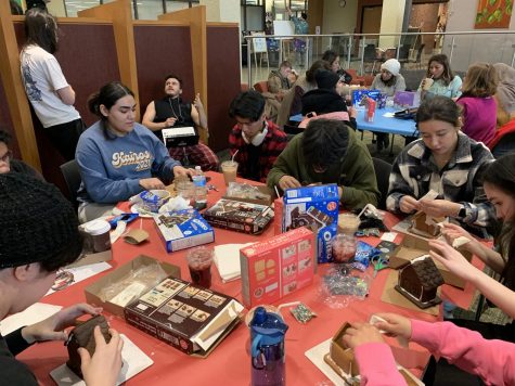 Group of students from different clubs sitting together and working on the variety of gingerbread houses.
