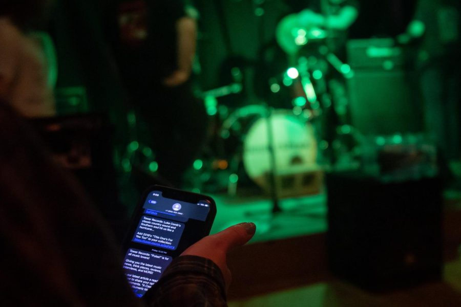 A concert attendee sits on their phone while a band plays on stage, displaying what many consider poor etiquette.