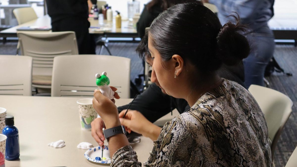 A student focuses while painting a green frog at the Pottery Painting and Pizza event hosted by New Student Connections on Sept. 21, 2021.