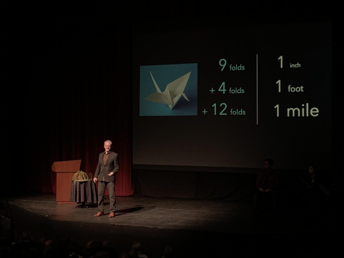 Robert Davies lecturing on the power of exponential growth through the example of folded paper during Rising Tide: The Crossroads Project at the Blizzard Theater on Oct 6, 2023.