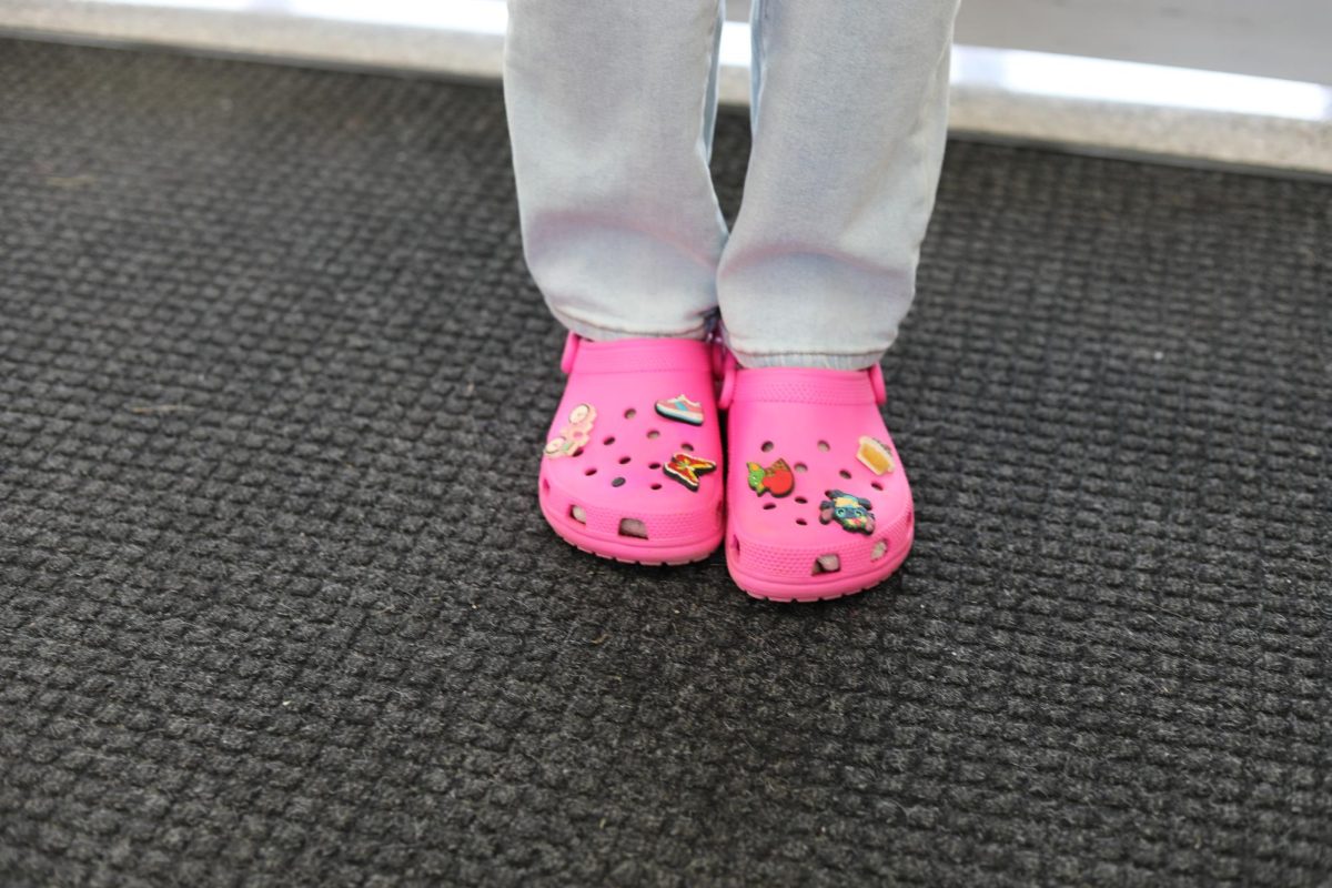 Close up of pink Crocs with charms on a black carpet.