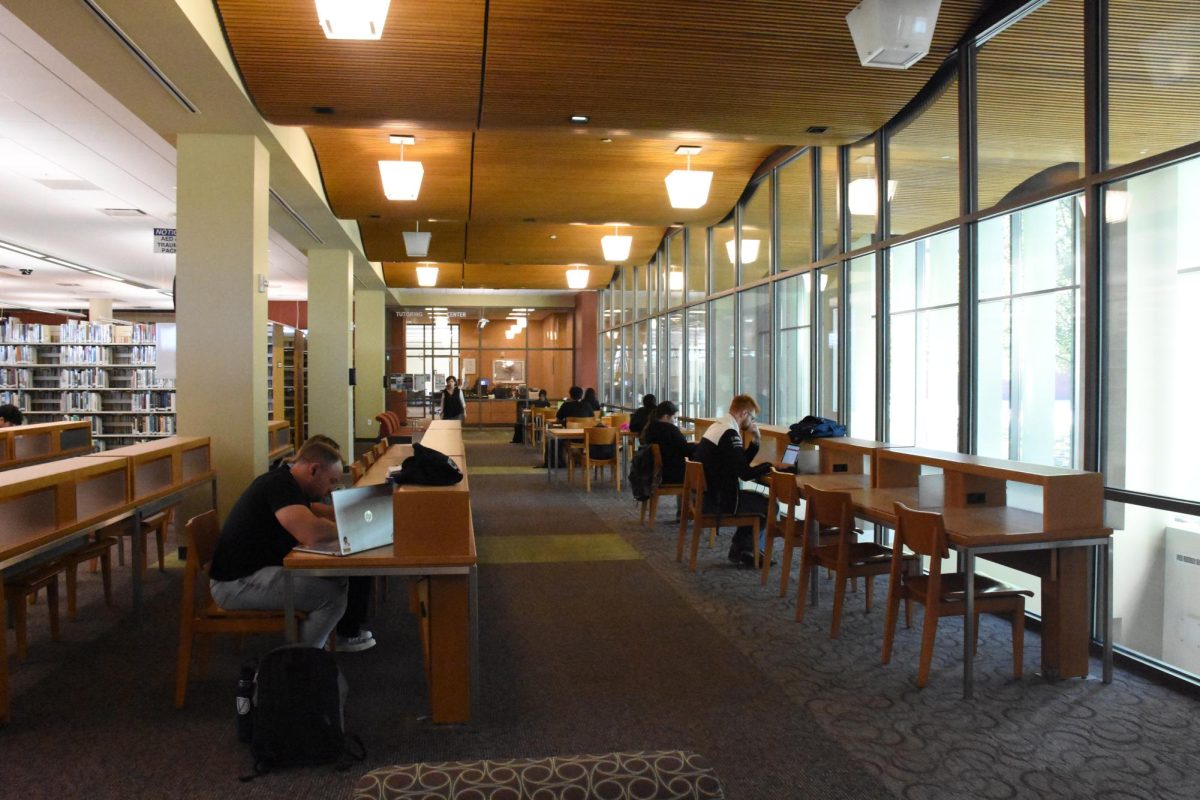 Students sit at a row of desks in a library.