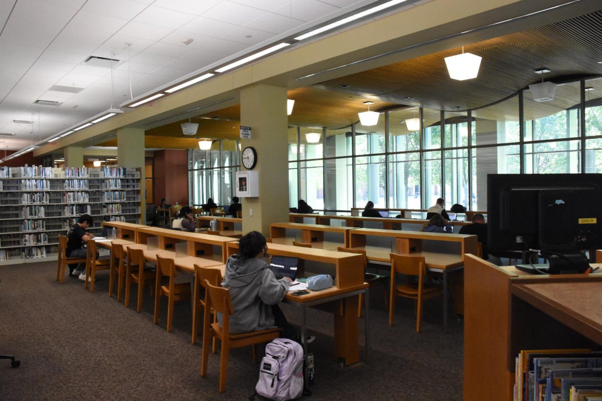 Students sit along a row of desks in a library.