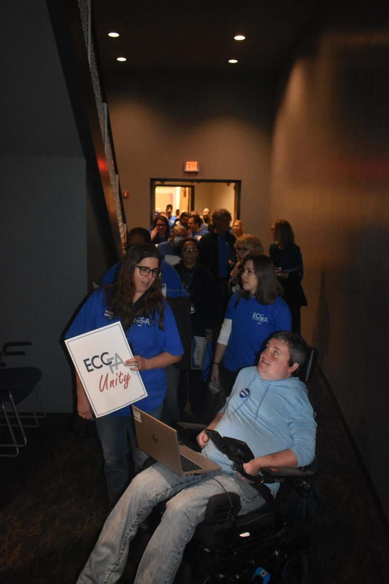 ECCFA members march into the Blizzard Theatre, holding signs and wearing matching blue t-shirts.