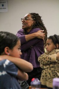 Dr. Brittany Barber wraps her arms around herself in the background while two young girls do the same in the foreground.